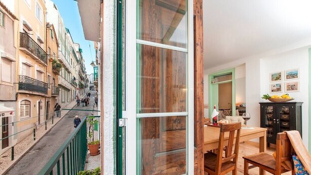 A narrow street view from a balcony with a wooden door, a dining area with a table and chairs, and a view of buildings on the street. - Cozy Apartment in Historical Lisbon by COZYSTAYS 2/5 (Lisbon)