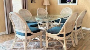 Een eethoek met een ronde glazen tafel, omringd door vier rieten stoelen met blauwe kussens.