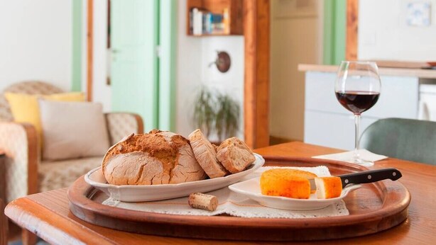 A dining table with a loaf of bread, a plate with a slice of cheese, and a glass of red wine. - Cozy Apartment in Historical Lisbon by COZYSTAYS 3/5 (Lisbon)