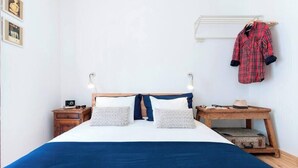 A neatly made bed with a blue blanket, two bedside tables with lamps, a wooden nightstand, and a wall-mounted coat rack with a plaid shirt. - Cozy Apartment in Historical Lisbon by COZYSTAYS 3/5 (Lisbon)