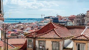 A coastal cityscape with traditional red-tiled rooftops, historic buildings, and a view of the sea. - Cozy Apartment in Historical Lisbon by COZYSTAYS 4/5 (Lisbon)