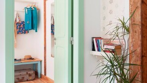 A room with a wooden floor, a teal door, a small table with a hat, a suitcase, and a shelf with books. - Cozy Apartment in Historical Lisbon by COZYSTAYS 4/5 (Lisbon)