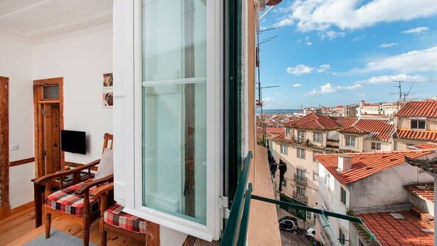 A balcony with a view of a town, a wooden chair, and a television on a stand. - Cozy Apartment in Historical Lisbon by COZYSTAYS 5/5 (Lisbon)