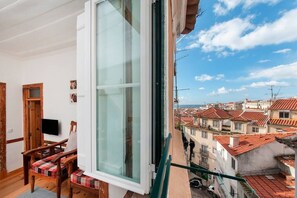Uma varanda com vista para uma cidade, uma cadeira de madeira e uma televisão sobre um suporte.