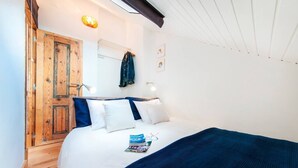 A bedroom with a wooden door, a bed with white and blue bedding, a magazine, and a pair of glasses on the bed. - Cozy Apartment in Historical Lisbon by COZYSTAYS 5/5 (Lisbon)
