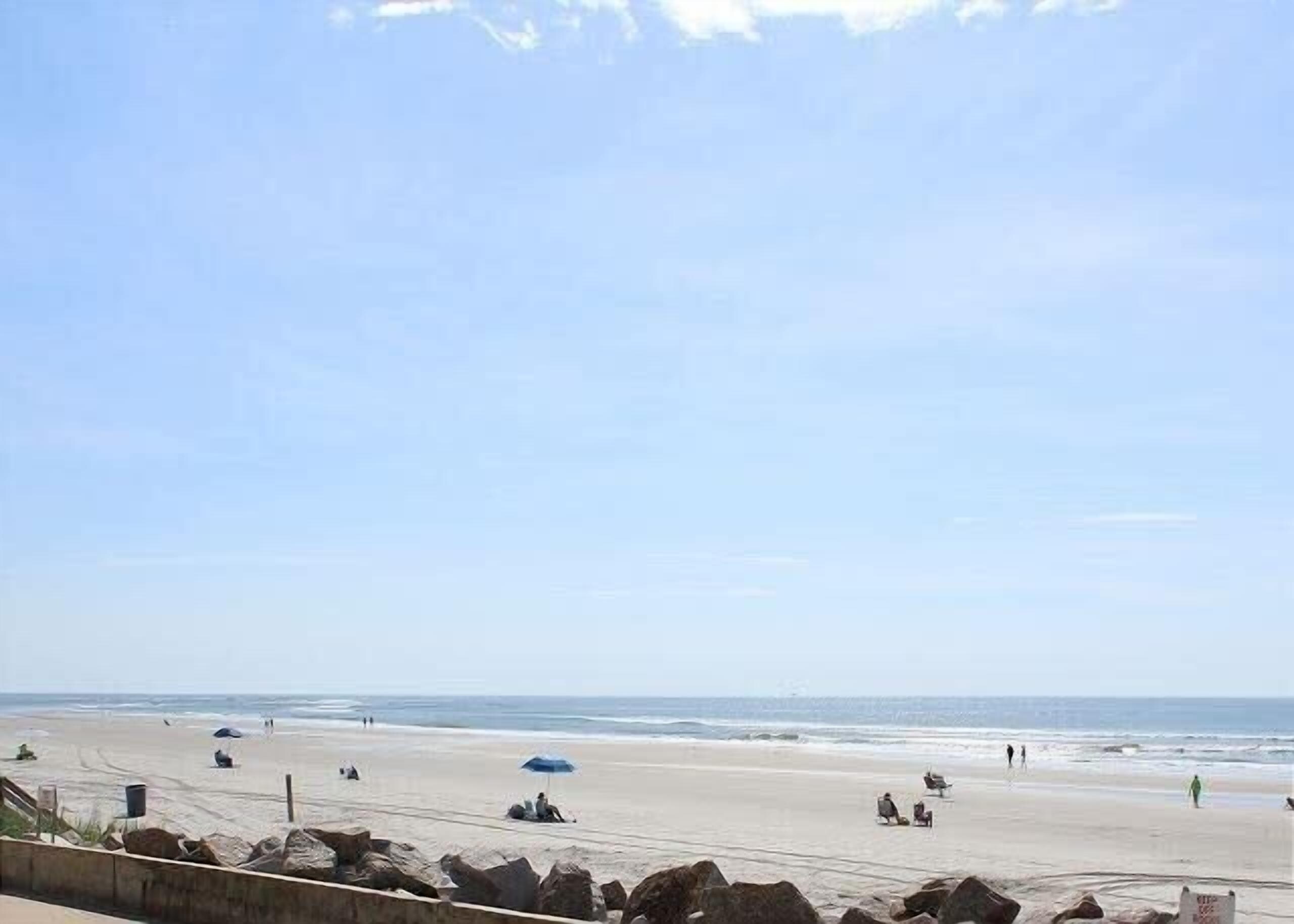 En strand med folk, en klar himmel och ett lugnt hav.