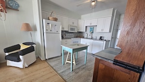 A compact kitchen with white cabinets, a small dining table, a refrigerator, and a ceiling fan. - Ocean View Villas E2 - The Sea Shed- Oceanview Condo (North Myrtle Beach)
