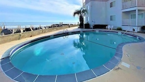 A swimming pool with a clear view of the ocean, a white building with balconies, and a sandy beach area. - Ocean View Villas E2 - The Sea Shed- Oceanview Condo (North Myrtle Beach)