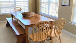 Une salle à manger avec une table en bois, quatre chaises, un banc et un panier en osier.