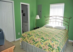 A bedroom with a floral bedspread, a metal bed frame, a bedside lamp, and a door leading to a bathroom.