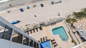 Een strand met parasols, ligbedden en een zwembad.