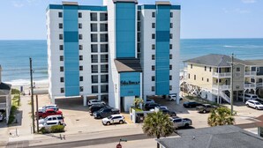 Een meerlaags hotel met een blauw-witte gevel, gelegen nabij een strand met zicht op de oceaan.