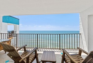 Un balcón con sillas y mesa de madera, con vistas a una playa y un cielo despejado.