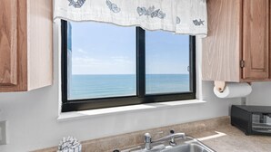 Een keuken met een raam met uitzicht op zee, een spoelbak en houten kastjes.