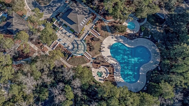 An aerial view of a property with a swimming pool, a circular driveway, and a building with a roof.