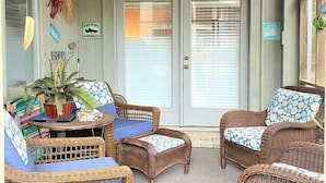 A covered porch with wicker furniture, a potted plant, and a door with a sign.