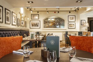 A restaurant with a wooden table set for dining, framed pictures on the walls, and a large window with a view. - The Crown Hotel, Boroughbridge, North Yorkshire (York)