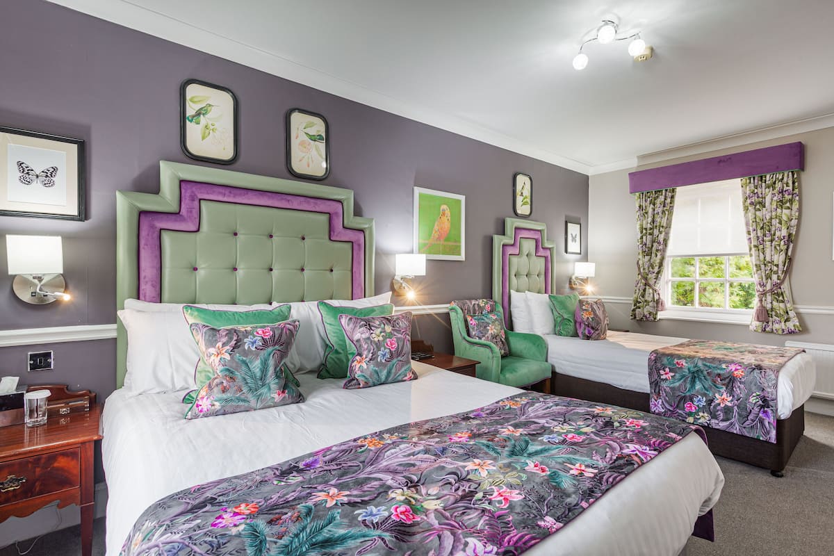 Ein Hotelzimmer mit zwei Betten, einem grünen gepolsterten Kopfteil, floralen Bettdecken und Bildern an den Wänden.