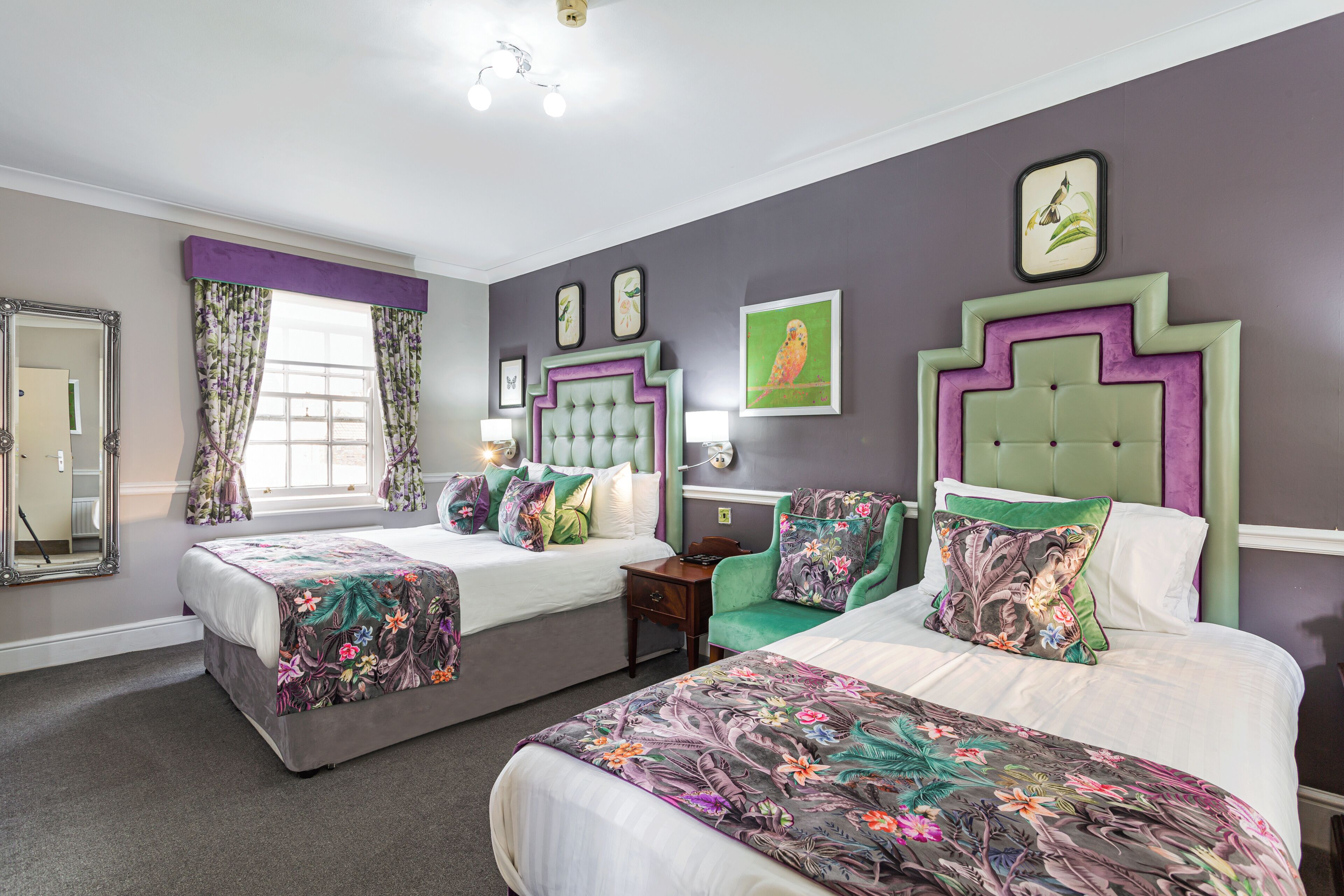 A hotel room with two beds, floral bedspreads, a mirror, and artwork on the walls.