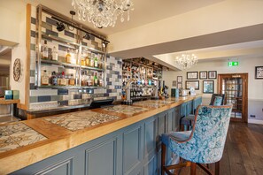 A bar area with a long counter, shelves with bottles, and a chandelier. - The Crown Hotel, Boroughbridge, North Yorkshire (York)
