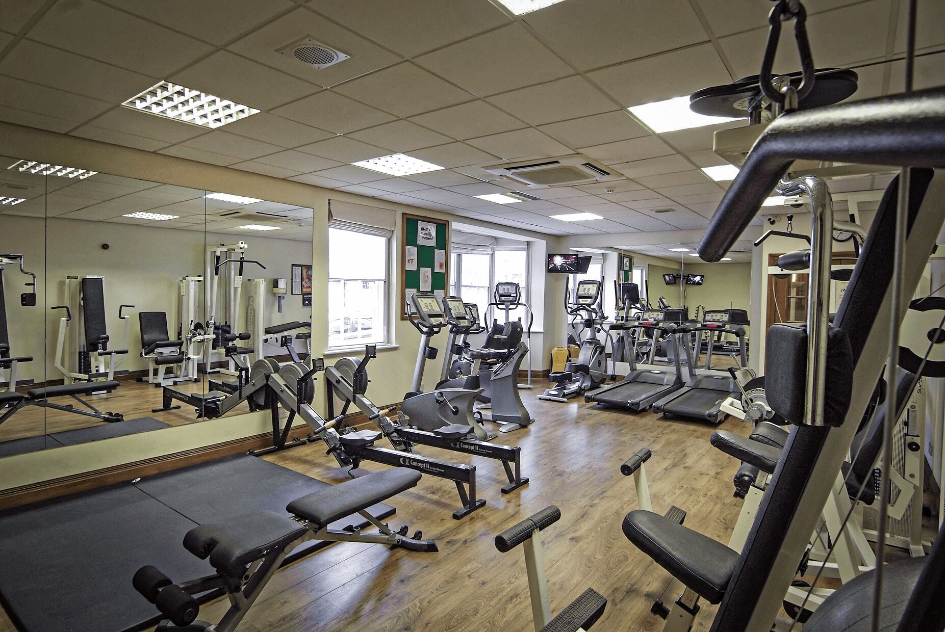 A gym with various exercise equipment, mirrors, and a wooden floor.