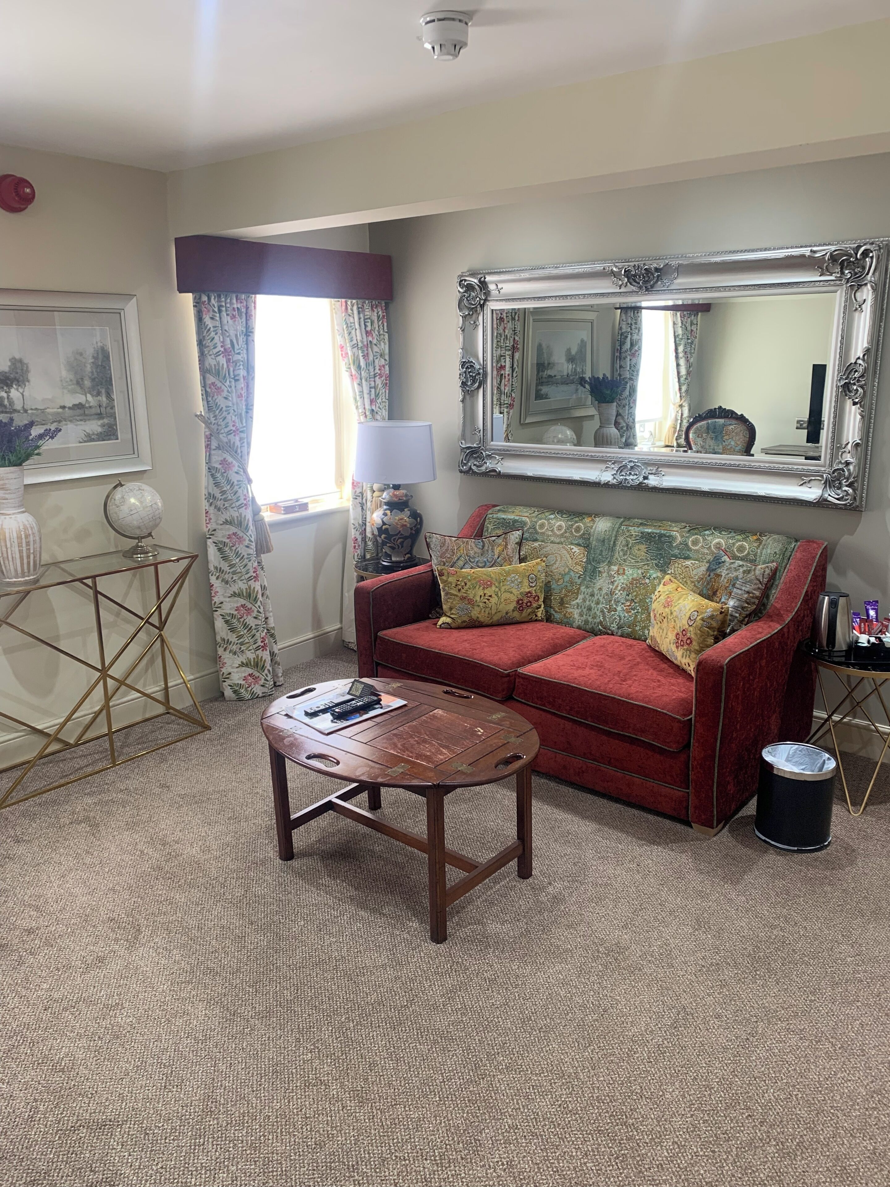 A living room with a red sofa, a round coffee table, a large mirror, and a globe on a side table.