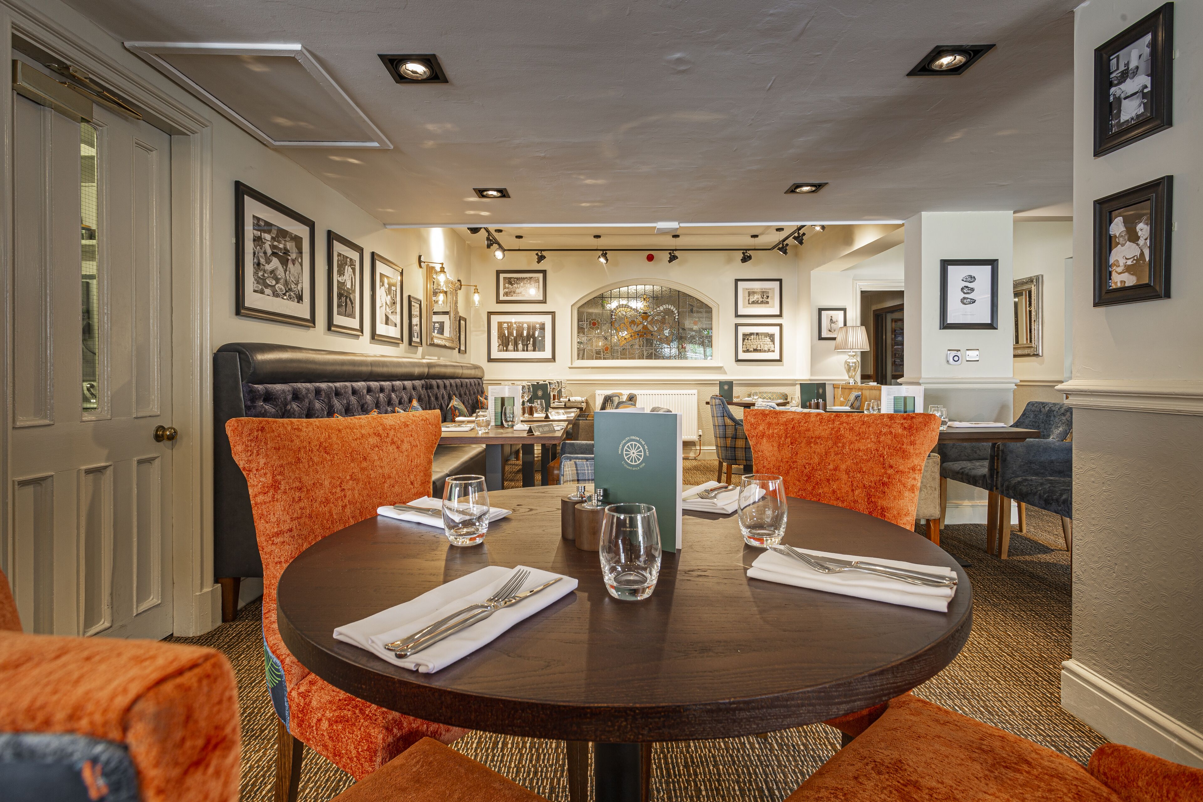 A dining area with a round table, orange upholstered chairs, and framed artwork on the walls.