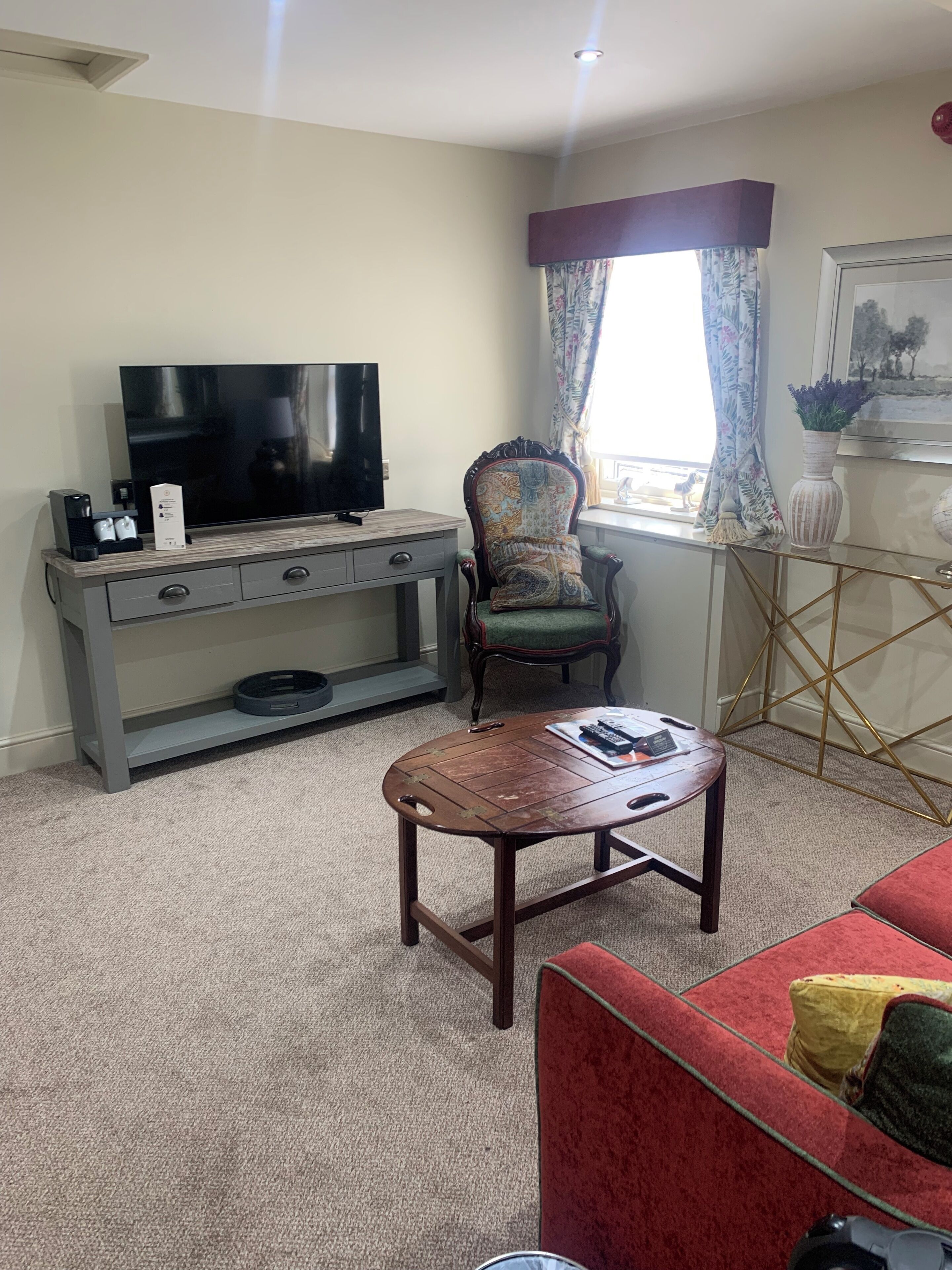 Una sala de estar con televisor, una silla, una mesa de centro y un sofá rojo.
