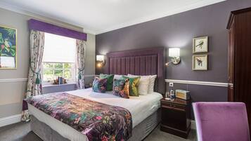 A bedroom with a large bed, a nightstand, a chair, and a window with curtains.