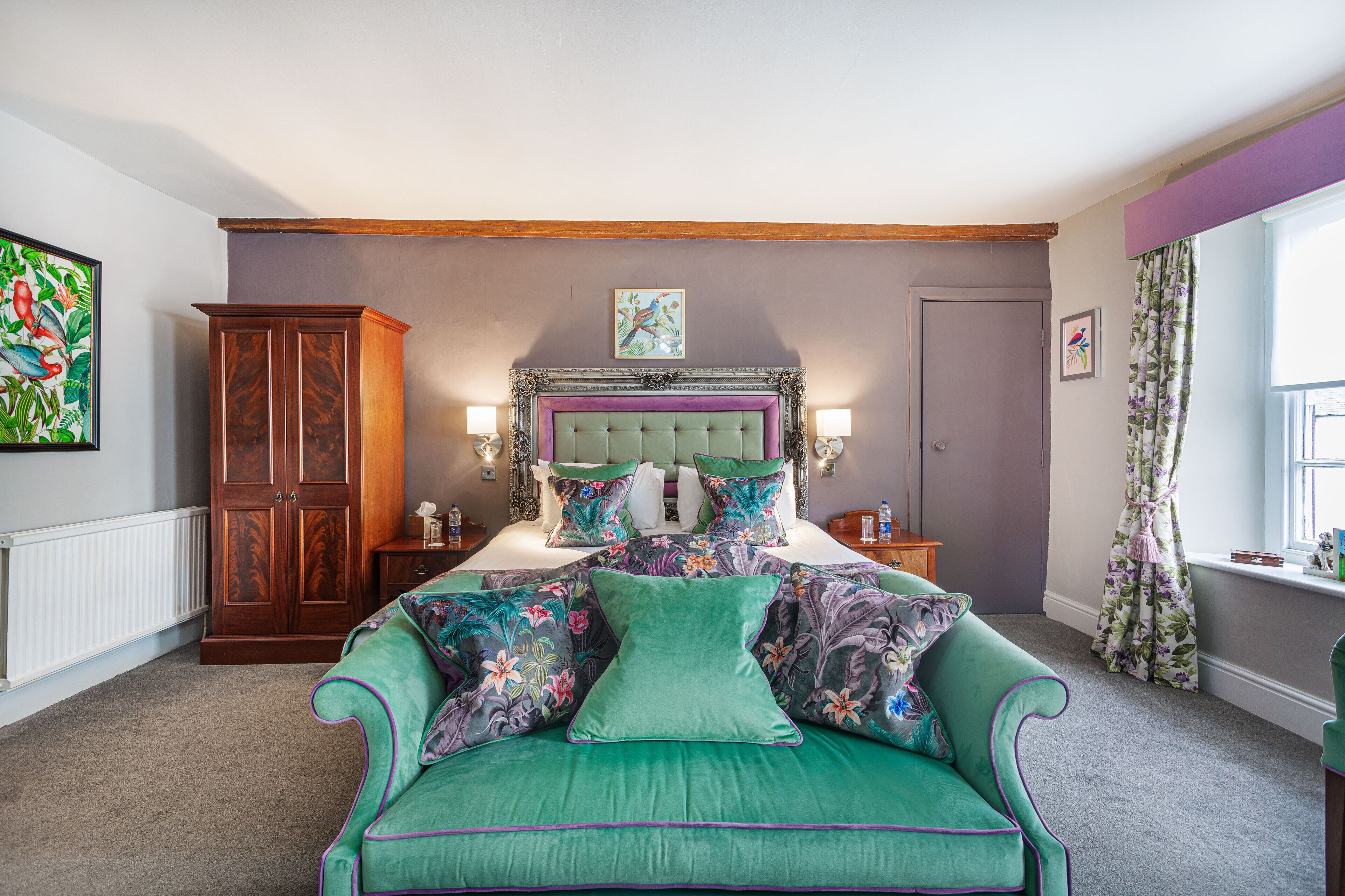 Een slaapkamer met een bed, een groene bank, een houten garderobe en kunst aan de muren.
