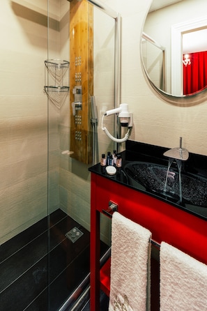 A modern bathroom with a glass-enclosed shower, a black sink with a red vanity, and a mirror with a red curtain reflection. - La Porte de Taksim (Istanbul)