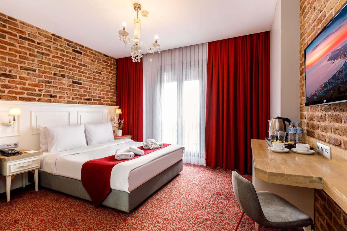 A hotel room with a brick wall, a large bed with white linens, a desk with a coffee maker, and a TV on the wall.