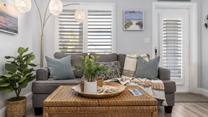 A living room with a grey sofa, a wicker coffee table, and a potted plant.