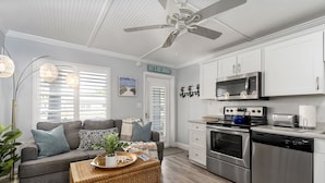 A modern kitchen with stainless steel appliances, a dining area with a grey sofa, and a ceiling fan.