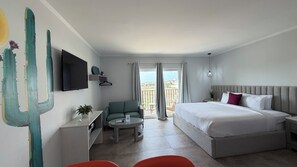Habitación de hotel con cama, escritorio, silla, televisor y balcón con cortinas.