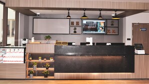 A reception desk with a digital screen, potted plants, and a coffee display.