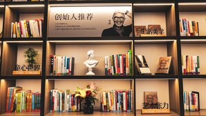A bookshelf with books, a bust sculpture, and a vase with flowers.