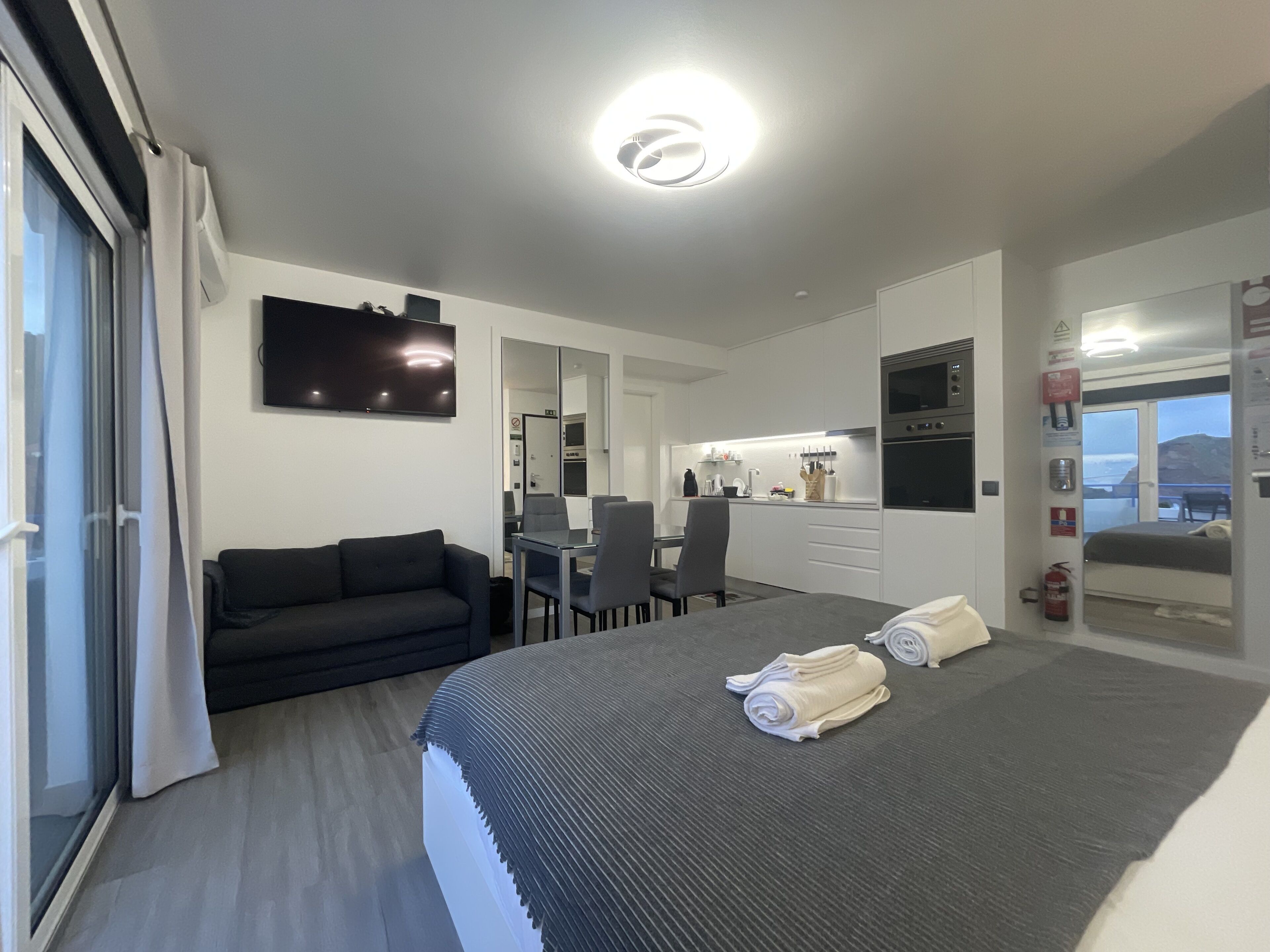 A modern hotel room with a bed, a sofa, a dining area, and a kitchen.
