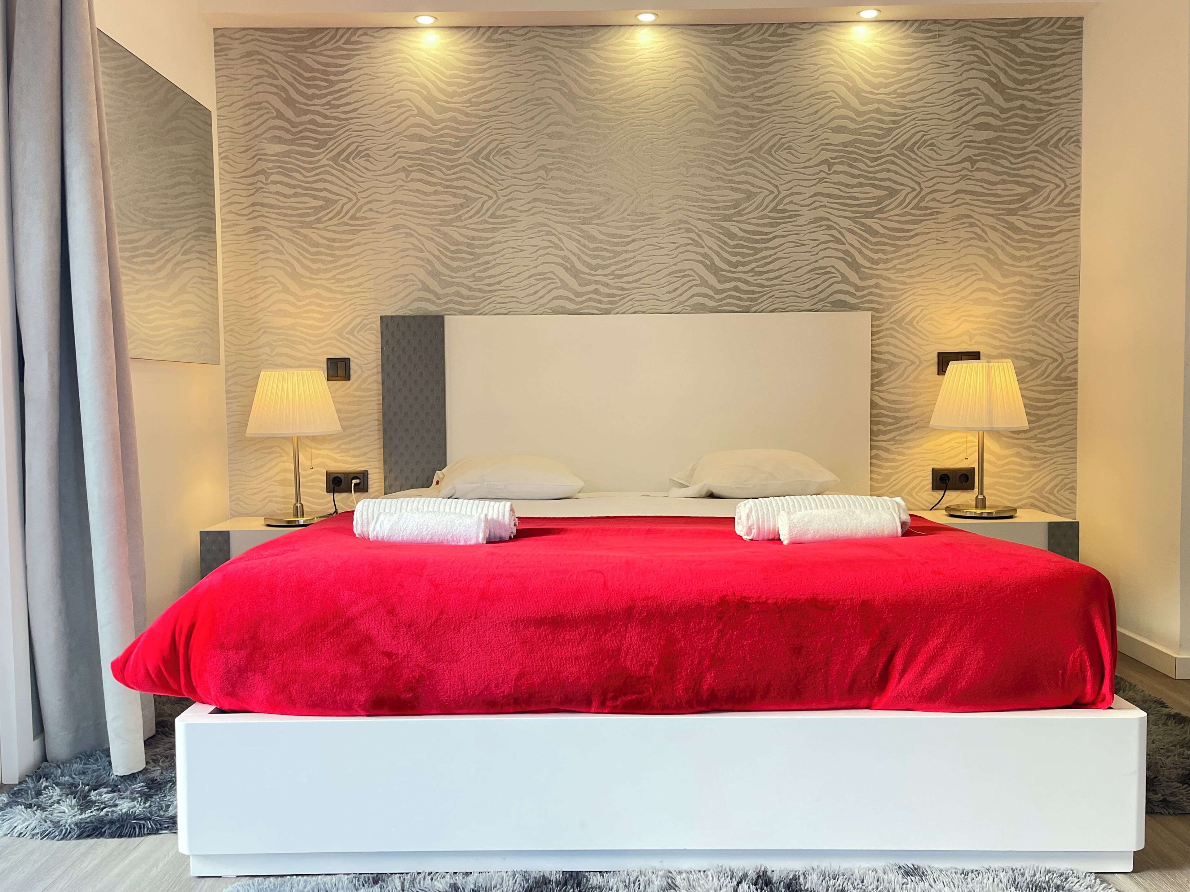 A modern hotel room with a large bed, two bedside lamps, and a patterned wall.