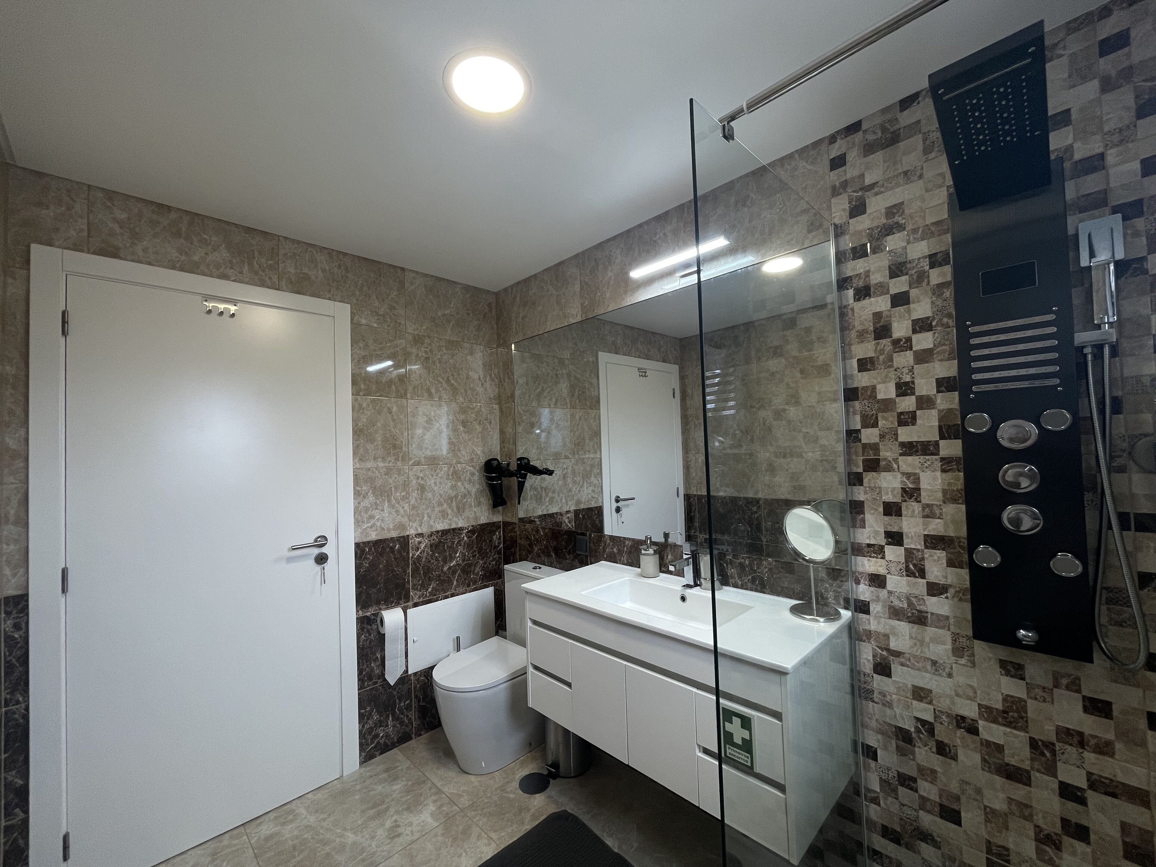Ein modernes Badezimmer mit Duschkabine aus Glas, einem weißen Waschbecken mit Spiegel und einer Toilette.