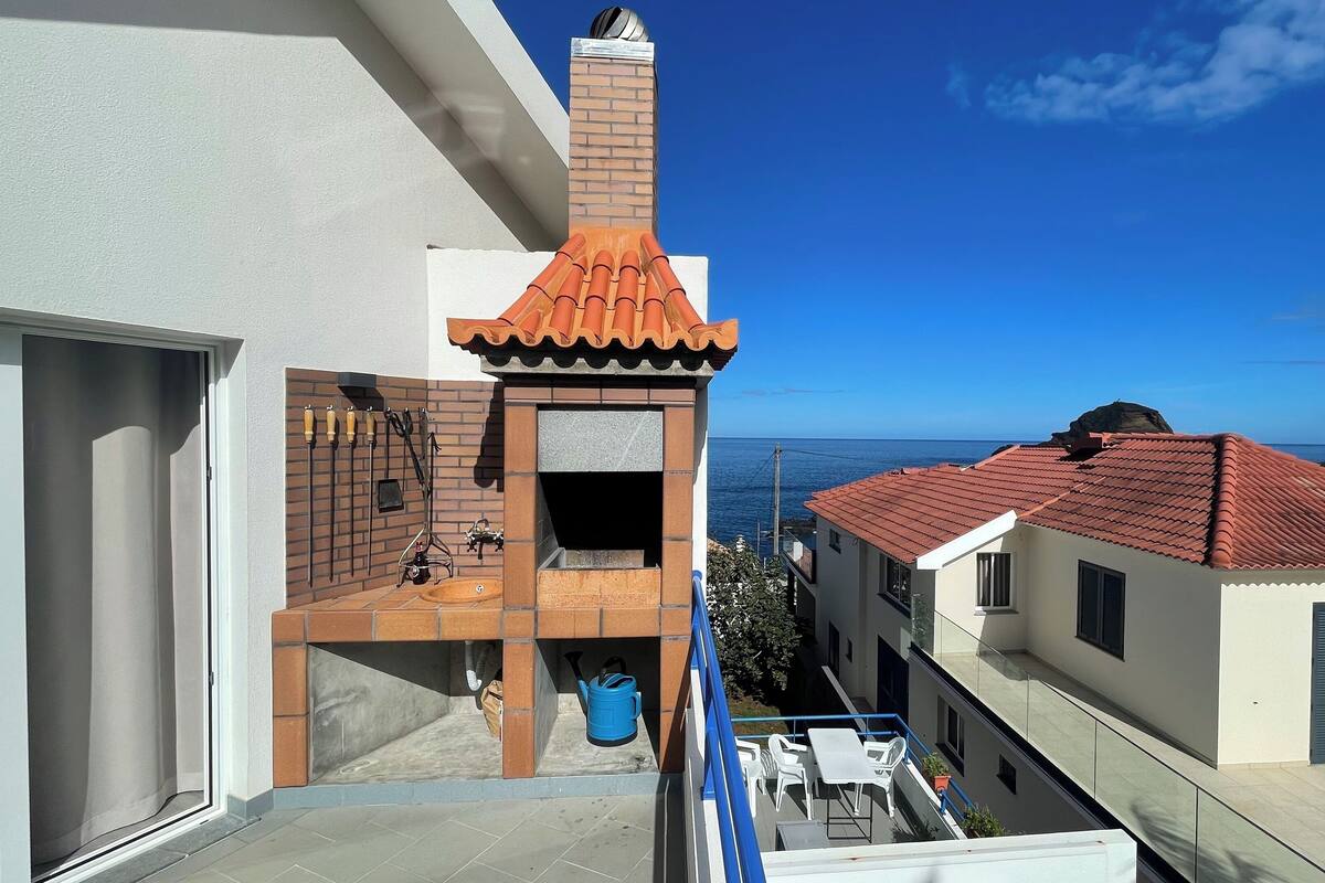 Un balcón con chimenea de ladrillo, paredes blancas y vista al mar.