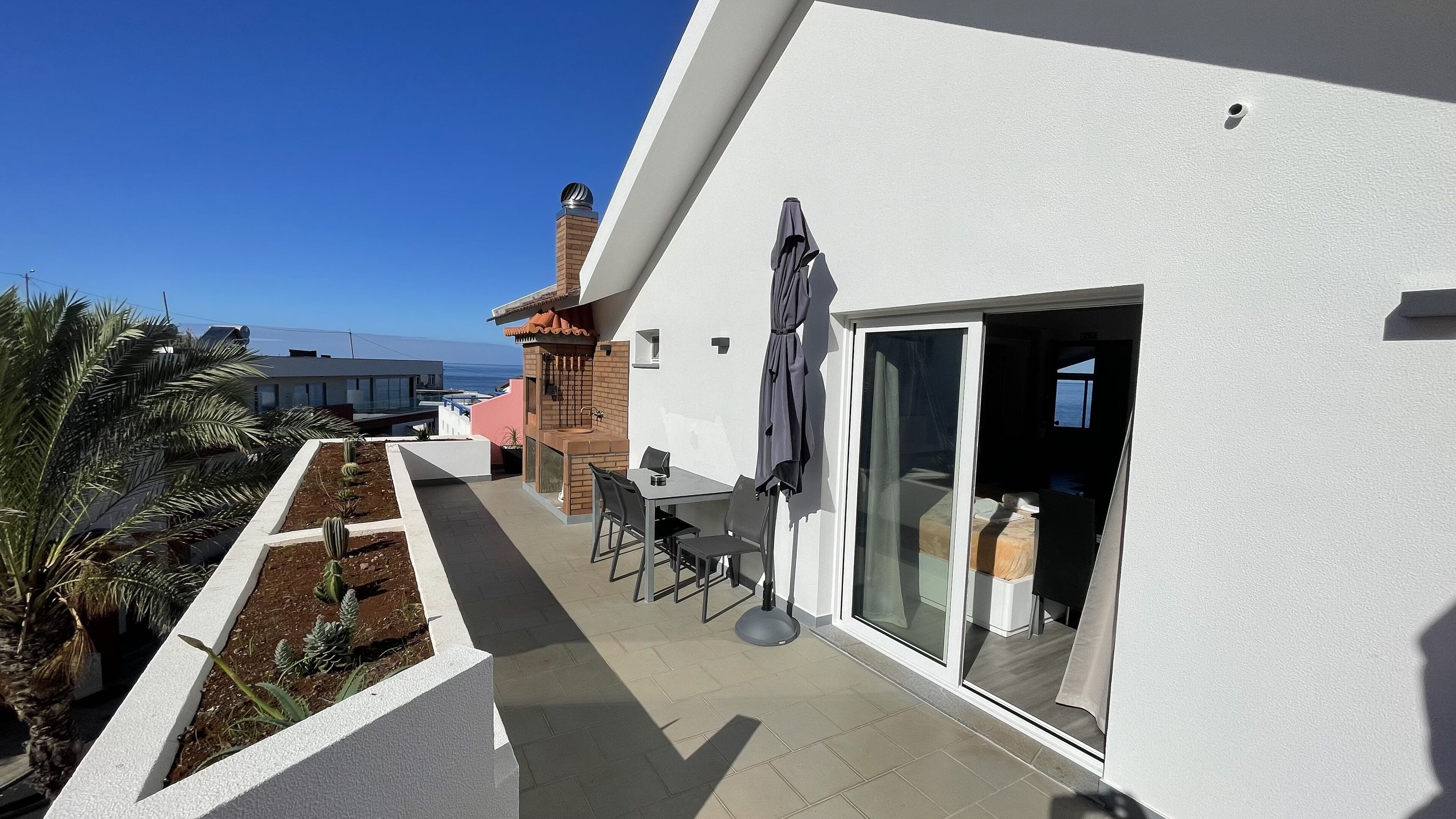 Een modern buiten terras met een tafel, stoelen, een barbecue en uitzicht op de oceaan.