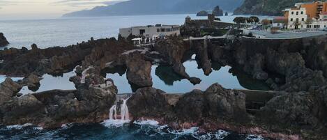 Zona costera con formaciones rocosas, una cascada y edificios con balcones con vistas al mar.
