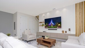 Een moderne woonkamer met een flatscreen tv aan de muur, een bank, een salontafel en een trap die naar een ander niveau leidt.