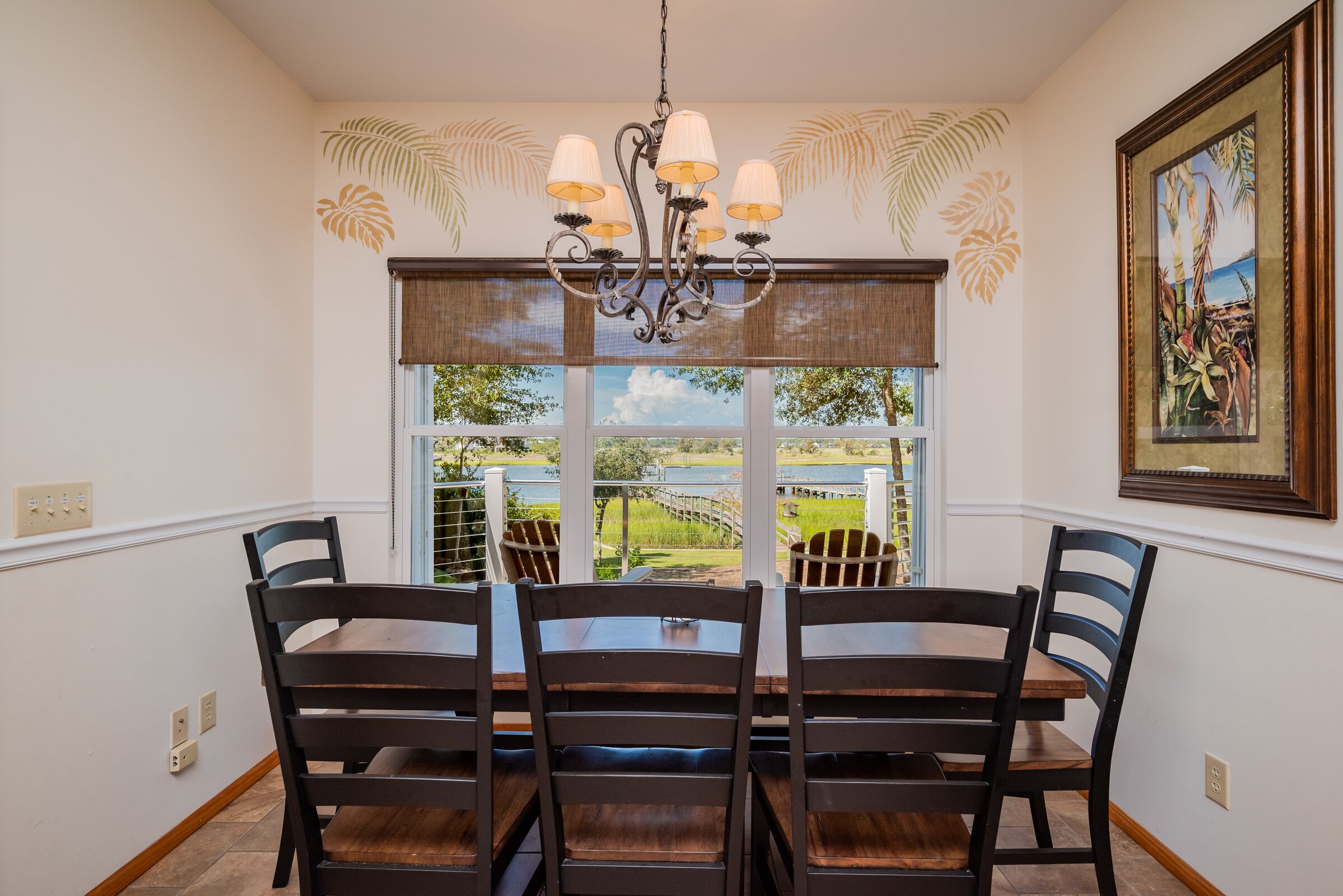 Un comedor con candelabro, sillas de madera, una mesa y un ventanal con vistas a zonas verdes.