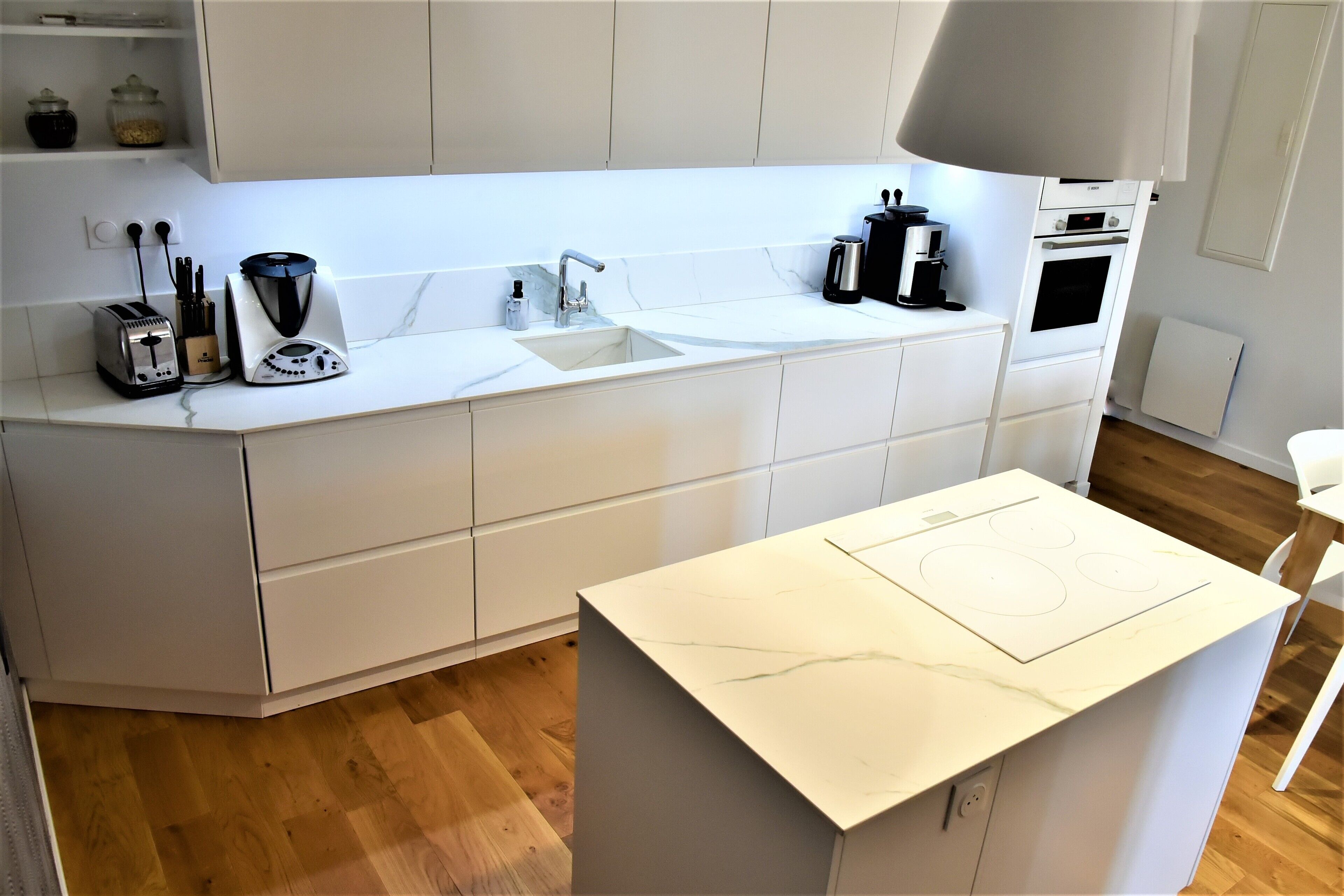 A modern kitchen with white cabinetry, a built-in sink, a stove, and a countertop with a coffee maker and toaster.