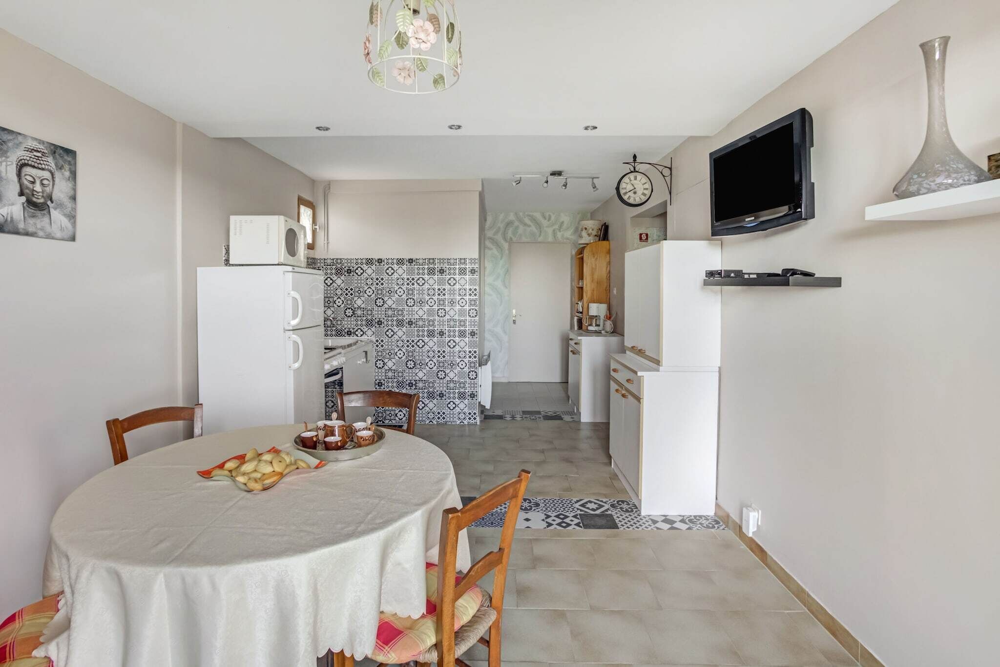 Een compacte keuken met moderne apparaten, een eethoek met een tafel gedekt voor twee personen, en een aan de muur bevestigde televisie.
