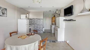 Een compacte keuken met moderne apparaten, een eethoek met een tafel gedekt voor twee personen, en een aan de muur bevestigde televisie.