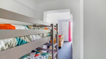 Een slaapkamer met een stapelbed, een houten ladder, een klein bureau en een raam met gordijnen.