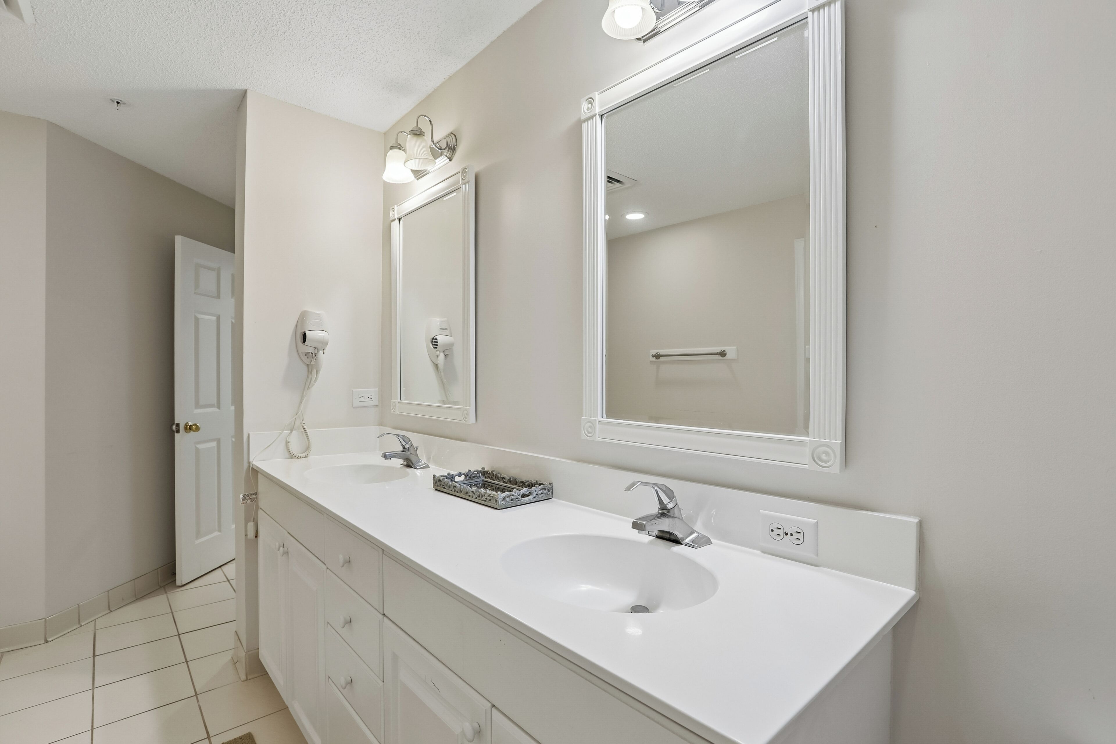 Une salle de bain avec un lavabo blanc, deux miroirs, un porte-serviettes et une porte.